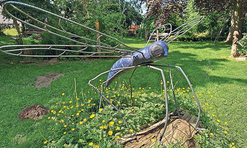 Libellenskulptur aus Metall im Garten auf einer Wiese.
