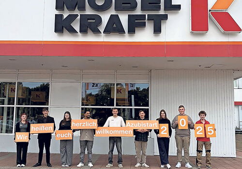 Azubis vor Möbel Kraft mit Willkommensschildern.