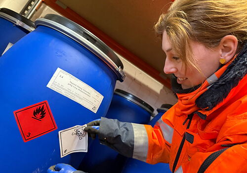 Person überprüft Gefahrensymbole auf blauen Fässern.