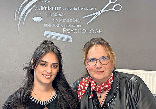 Zwei Frauen vor einer Friseur-Wandgestaltung.