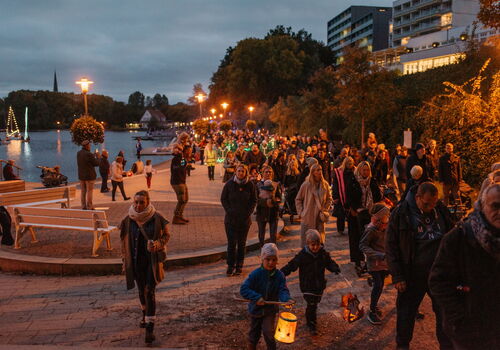Menschen mit Laternen spazieren abends am Fluss.