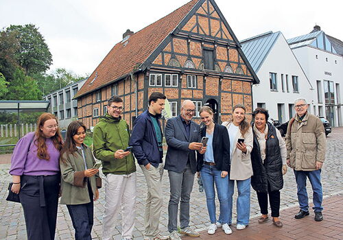 Gruppe steht lächelnd vor einem Fachwerkhaus und schaut auf Handys.