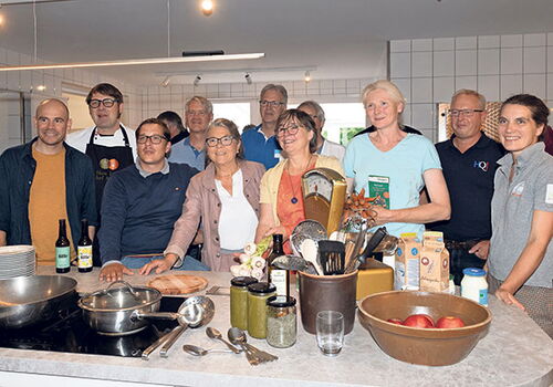 Gruppe von Menschen in einer Küche, Kochutensilien auf dem Tisch.