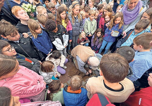 Kinder versammeln sich um eine Person bei einer Zeremonie im Freien.