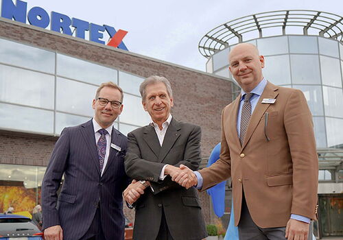 Drei Männer vor einem Gebäude mit Nortex-Logo