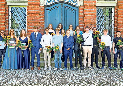 Gruppenbild von Schülern mit Sonnenblumen vor einem Gebäude.
