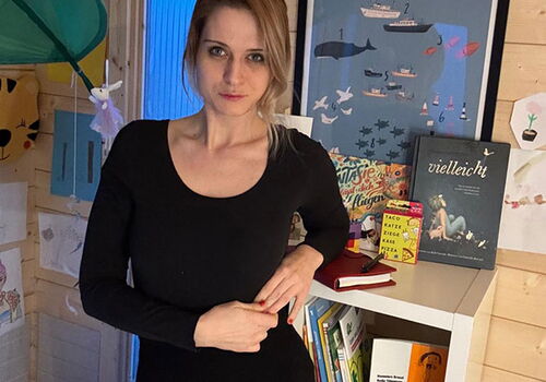 Person in einem Zimmer mit Büchern und Bildern an der Wand.