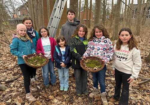 Gruppe von Kindern im Wald mit Körben voll Blätter.