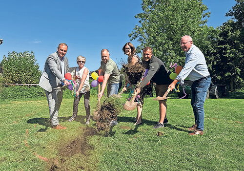 Gruppe feiert Spatenstich mit bunten Schaufeln.