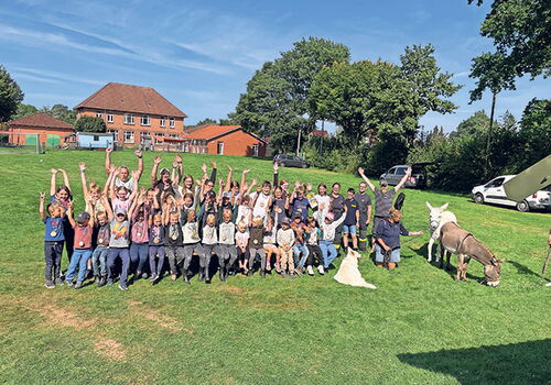Kindergruppe auf Wiese mit Tieren und erhobenen Armen