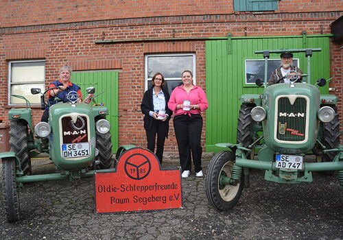 Personen posieren mit Oldtimer-Traktoren vor Ziegelwand.
