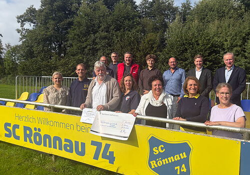 Gruppe posiert mit Scheck vor SC Rönnau 74 Schild.