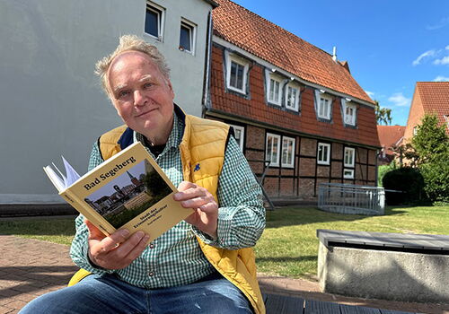 Mann liest Buch vor traditionellem Fachwerkhaus.