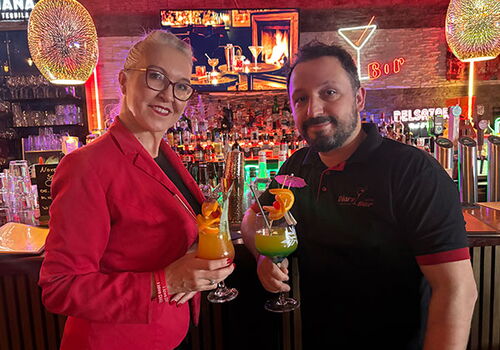 Zwei Personen halten Cocktailgläser in einer Bar.