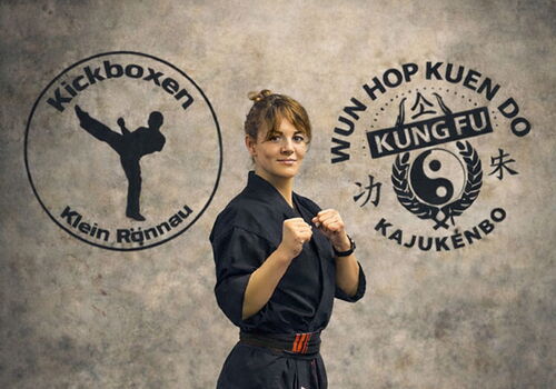 Person in Kampfkunst-Uniform posiert vor Vereinslogos.