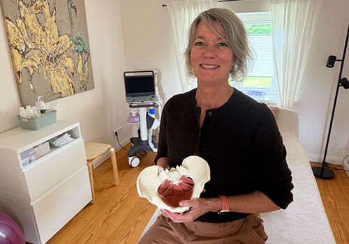 Frau mit anatomischem Beckenmodell in Behandlungszimmer.
