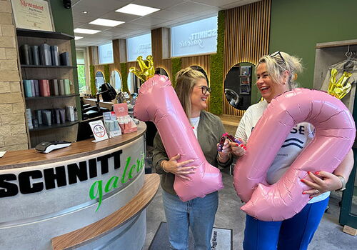 Zwei Frauen halten rosa Luftballons mit der Zahl 10 in einem Salon.