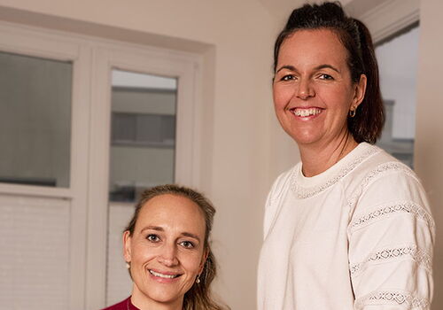 Zwei Frauen lächeln, eine hält einen Karton.