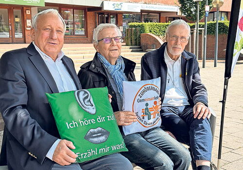 Drei Personen auf einer Bank mit Kissen, die Texte tragen.