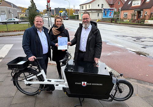 Drei Personen mit Lastenrad vor Straßenszene.