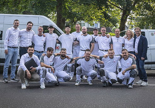 Gruppe von 16 Personen vor zwei Transportern posiert.