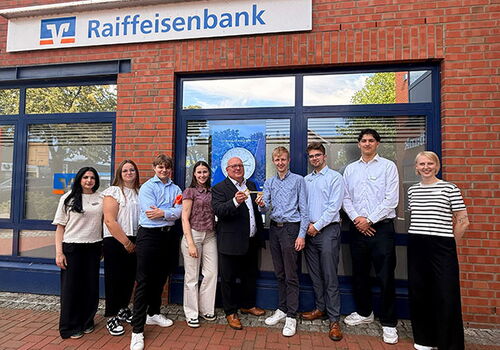Gruppe vor einer Raiffeisenbank-Filiale posiert lächelnd.