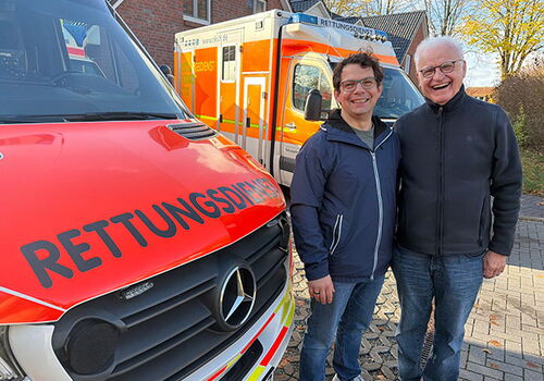 Zwei Männer vor Rettungswagen und Gebäude.