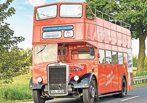 Roter Doppeldeckerbus auf einer Landstraße.
