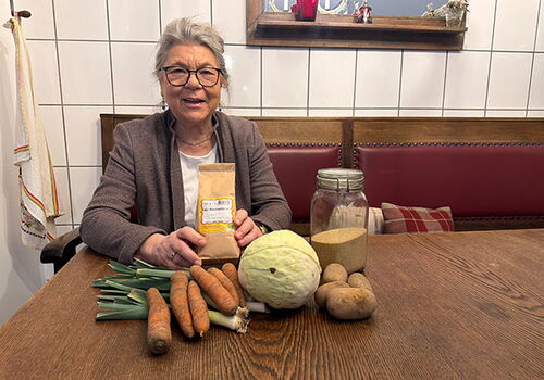 Frau mit Suppengrün und Glas auf Holztisch.
