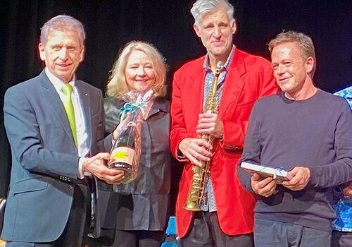 Gruppe von vier Personen posiert mit Geschenken auf einer Bühne.