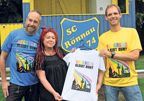 Drei Personen halten ein buntes T-Shirt vor einem SC Rönnau Schild.