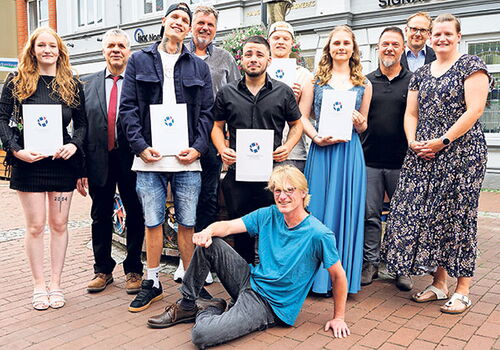 Gruppe von Menschen posiert auf Pflastersteinen mit Urkunden.