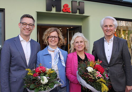 Vier Personen mit Blumensträußen vor einem Geschäft.