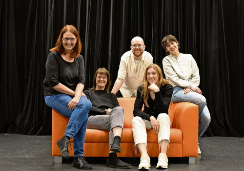Fünf Personen sitzen auf einem orangefarbenen Sofa.