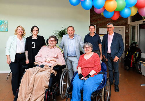 Gruppe posiert unter bunten Luftballons in einem Raum.