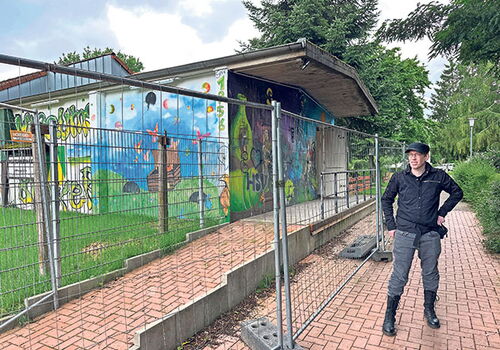 Mann neben einem bunt bemalten Gebäude hinter einem Zaun.
