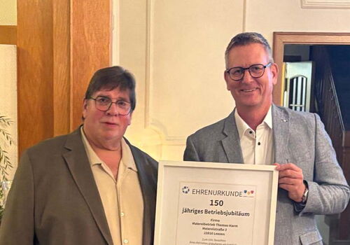 Zwei Männer halten eine Ehrenurkunde für 150 Jahre Jubiläum.