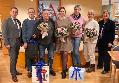 Sieben Personen posieren mit Geschenken und Blumensträußen.