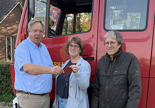 Drei Personen stehen vor einem roten Feuerwehrwagen.