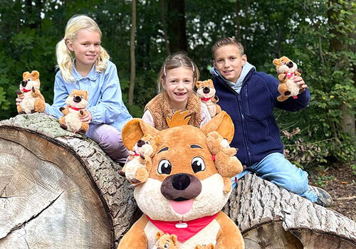 Kinder sitzen mit Kuscheltieren auf Baumstämmen im Wald.