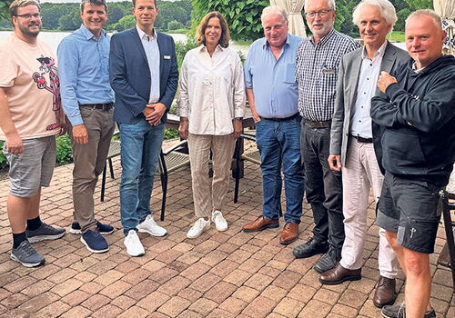 Gruppe von acht Personen posiert im Freien auf einer Terrasse.