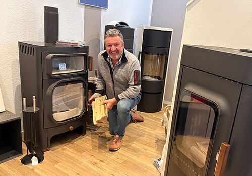 Mann mit Brennholz vor Kaminofen im Showroom