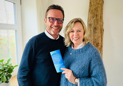 Ein Paar hält ein blaues Heft vor einem Fenster.