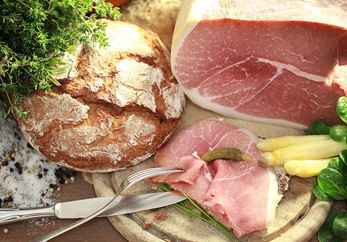 Brot und Schinken auf einem Tisch mit Kräutern.