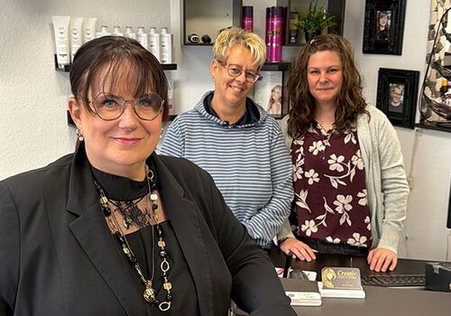 Drei Frauen in einem Friseursalon, lächelnd in die Kamera.
