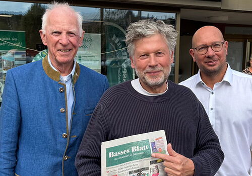 Drei Männer vor Basses Blatt Büro, einer hält Zeitung.