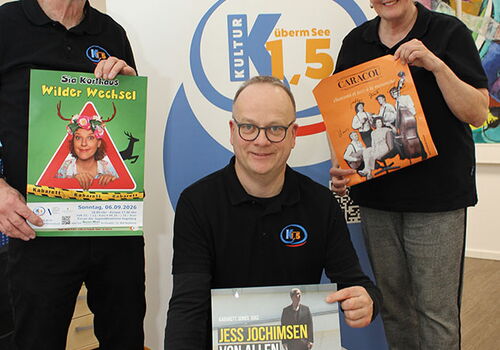 Drei Personen halten Werbeplakate vor einem Banner.