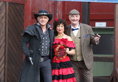 Drei Personen in Western- und Kostümkleidung posieren lächelnd.