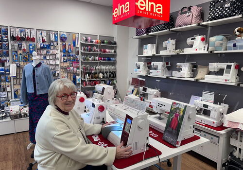 Frau sitzt an Nähmaschine in einem Geschäft voller Zubehör.