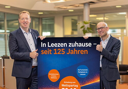 Zwei Männer halten ein Plakat zum Weltspartag in einer Bankfiliale.